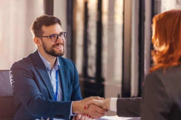Two people shaking hands during a business meeting, with one smiling across a table.