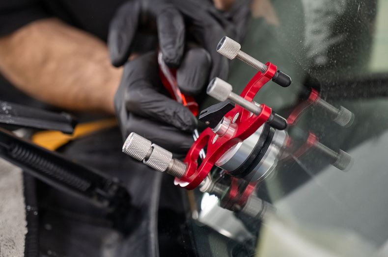 Gloved hand using a red tool on a car windshield crack repair area