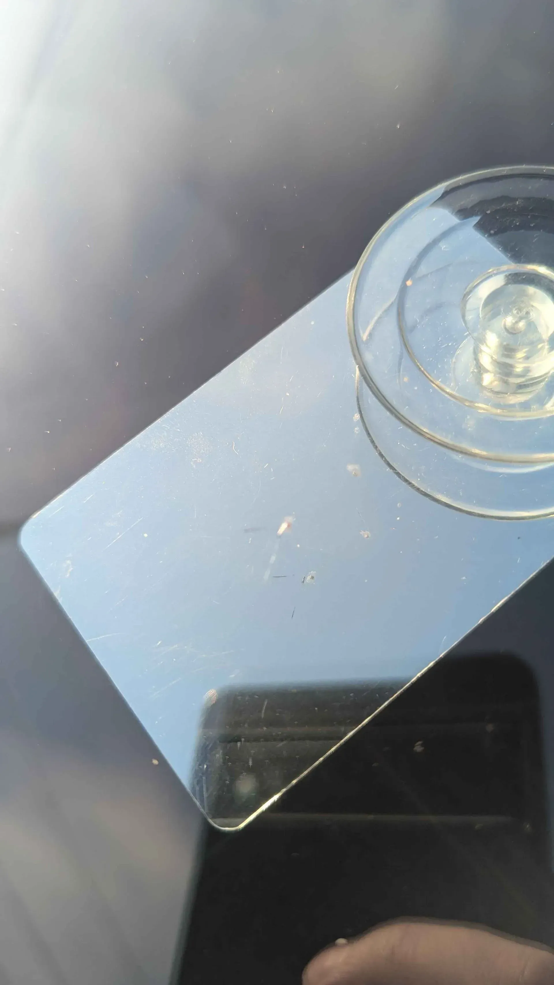A glass on a reflective surface beside a smartphone, seen in bright sunlight.