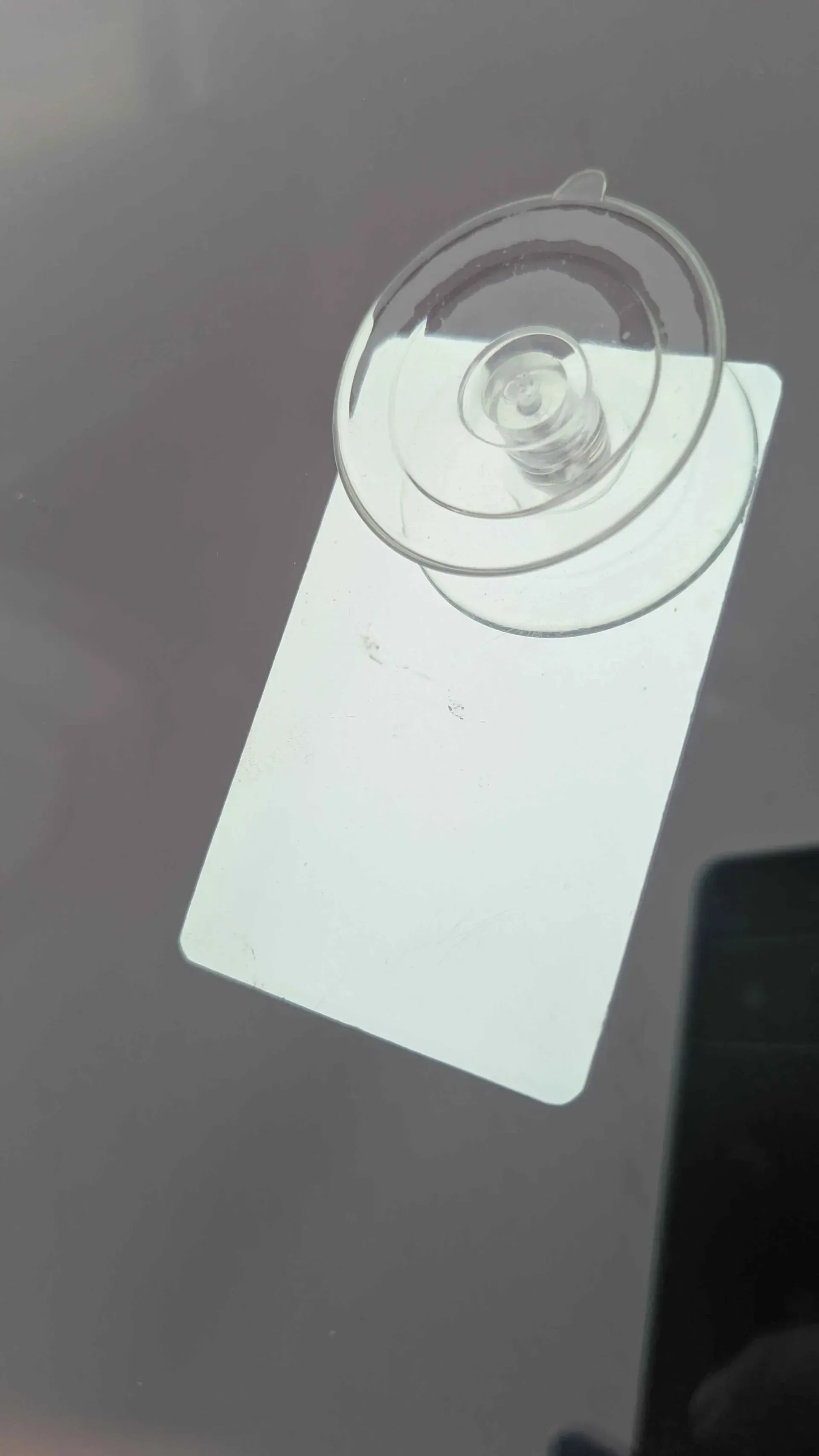 White rectangular tag hanging from a suction cup on a gray surface, viewed at an angle