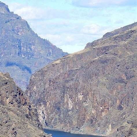 Mountain canyon with steep rocky cliffs and a river below under a pale blue sky
