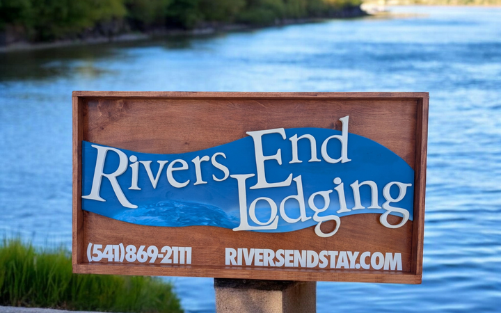 Wooden Rivers End Lodging sign by a river, with white text on blue background.