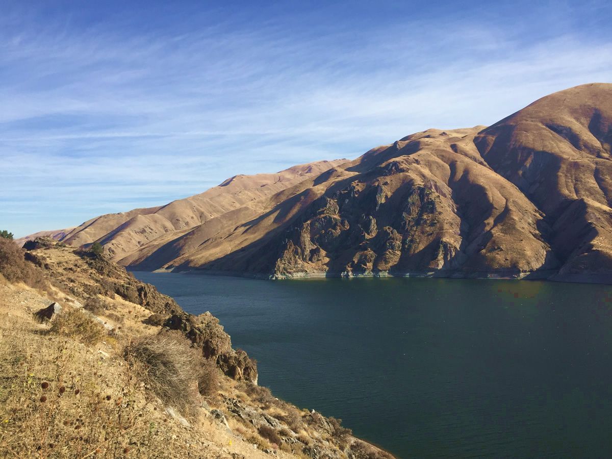 Sunlit brown mountains beside a dark blue lake under a clear sky
