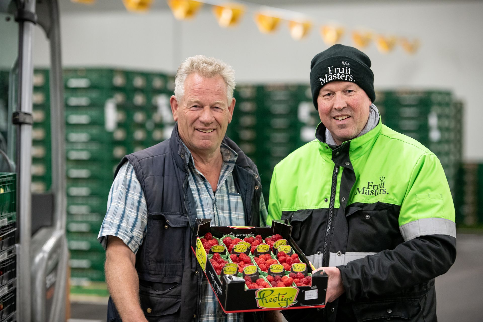 Twee mannen staan naast elkaar met een doos aardbeien in hun handen.