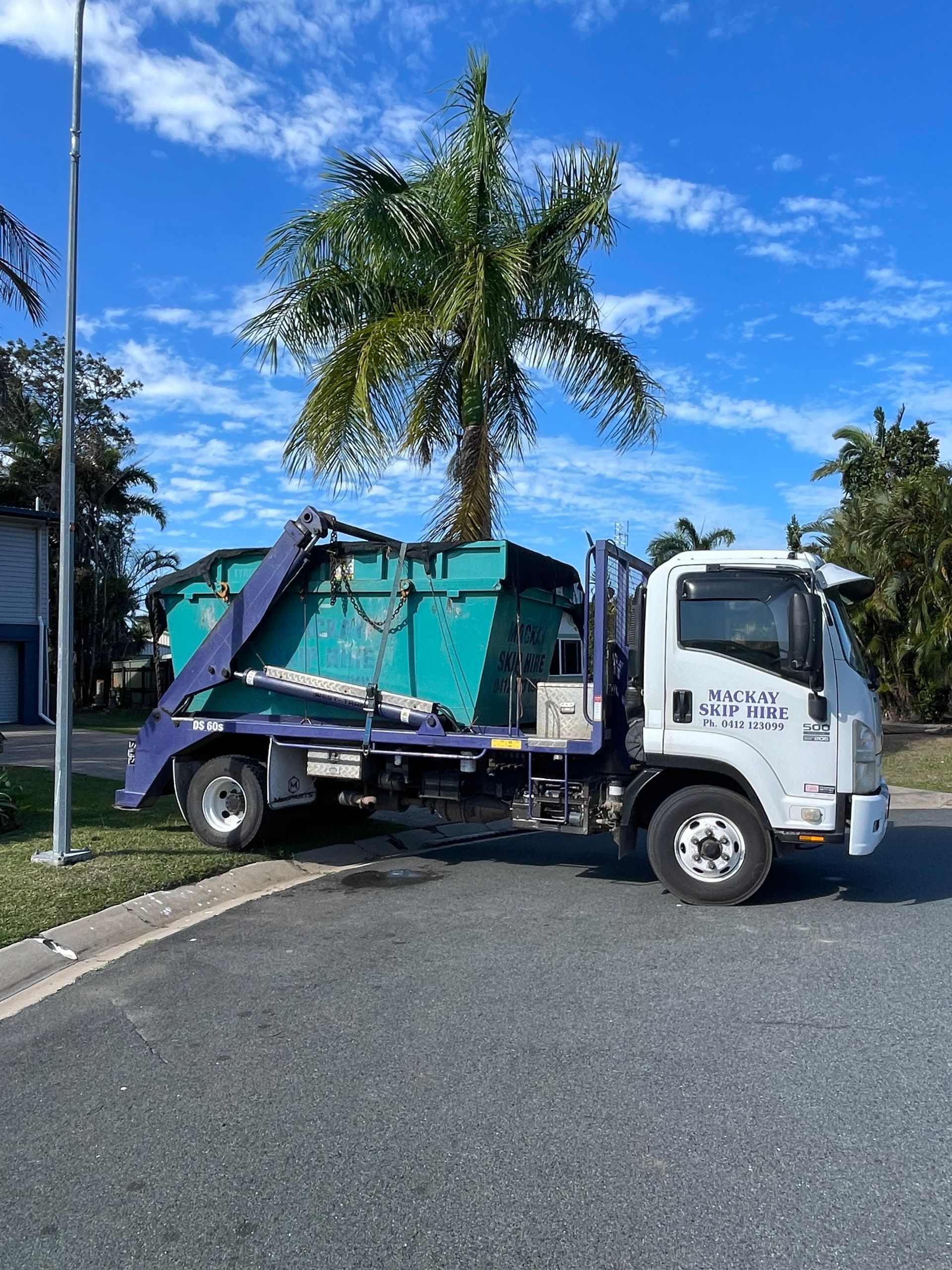 A Blue Waste Container on a Truck, Parked on a Paved Road Under a Bright Blue Sky — Mackay Skip Hire In Andergrove, QLD