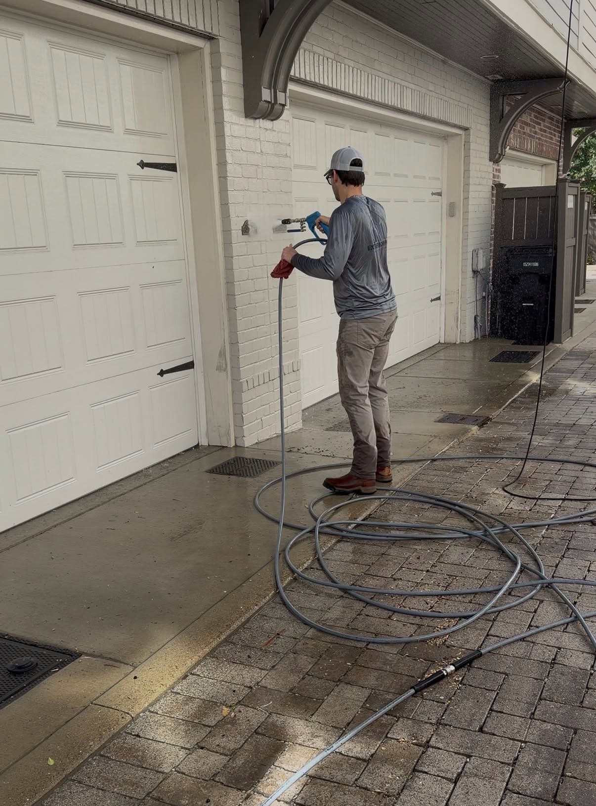 Person pressure-washing garage doors and driveway with coiled hose nearby