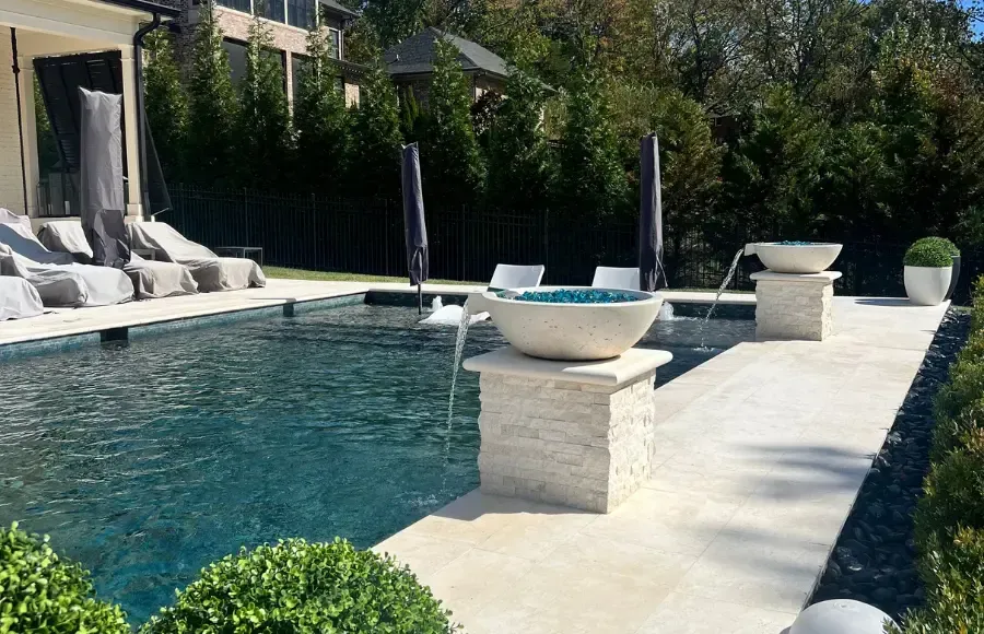 Modern backyard pool with stone deck, lounge chairs, and planters in bright sunlight