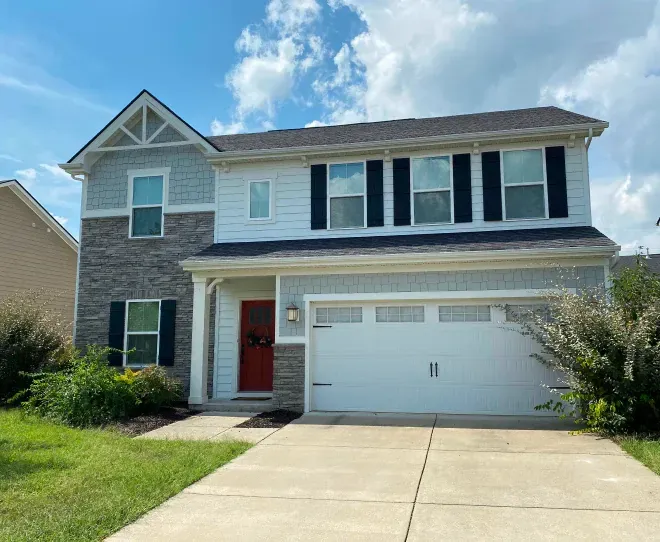 Two-story suburban house with white siding, brick accents, red front door, and a two-car garage