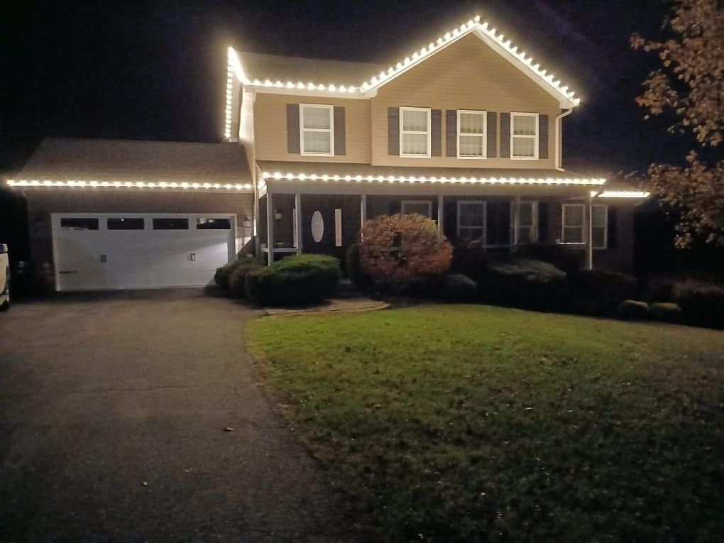 Two-story house and garage outlined with white holiday lights at night.
