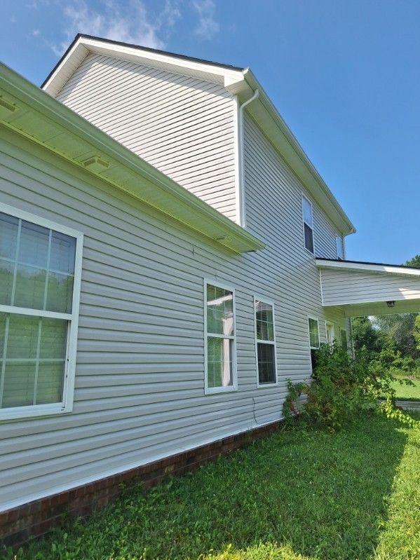 Side view of a white house with vinyl siding, windows, and green lawn under a blue sky.