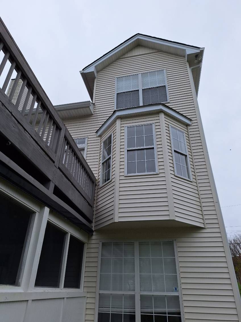 Gray-sided house with a bay window beside a dark wooden deck under an overcast sky