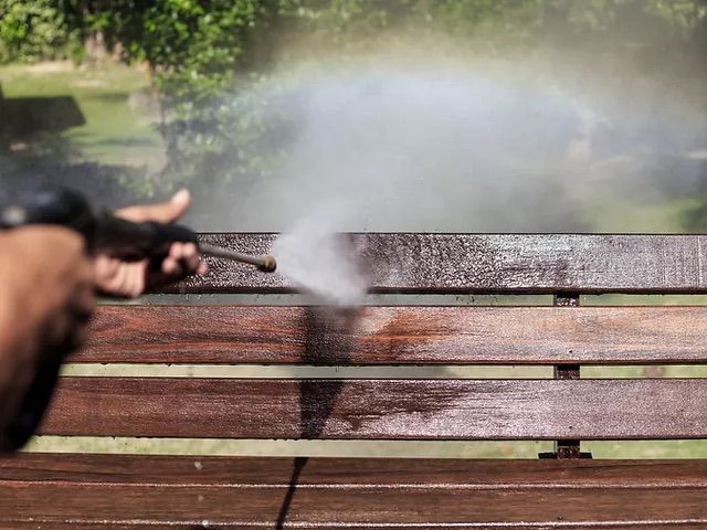 Person firing a handgun toward a wooden bench, with smoke and water spraying in the background