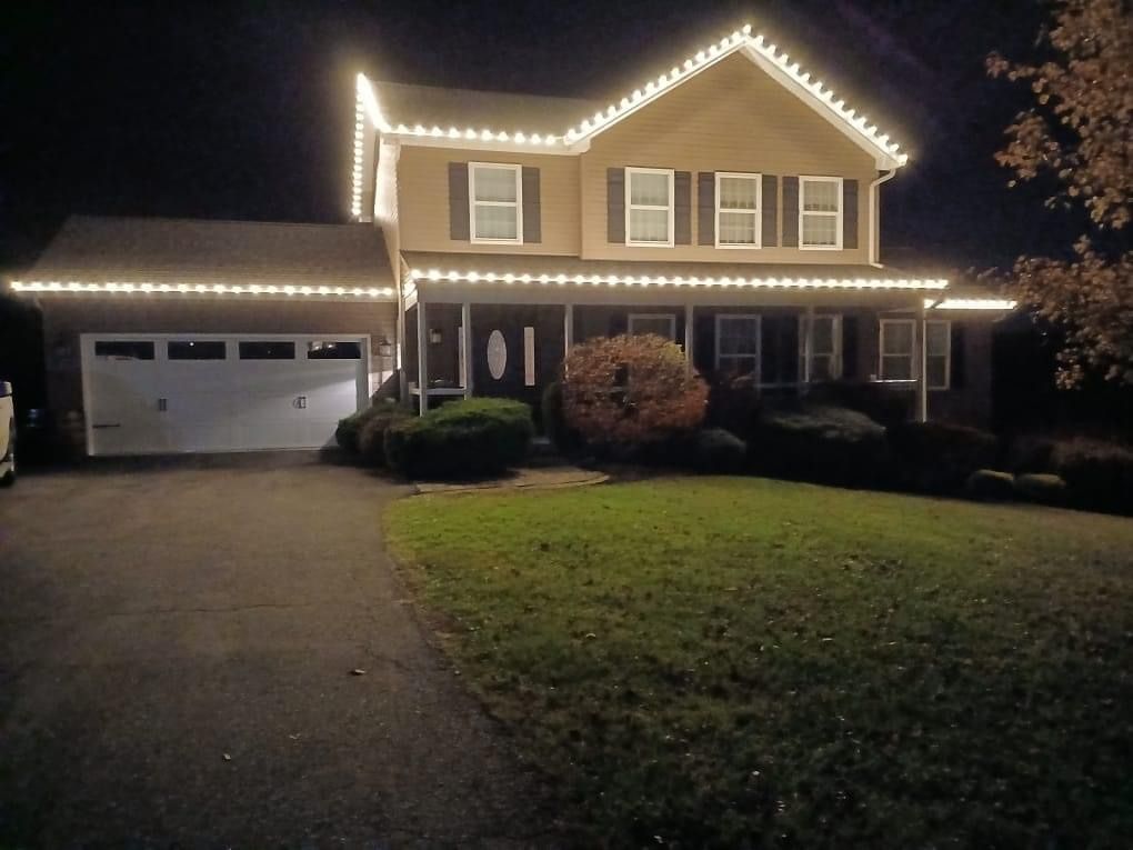 Two-story house at night with white holiday lights outlining the roof and garage