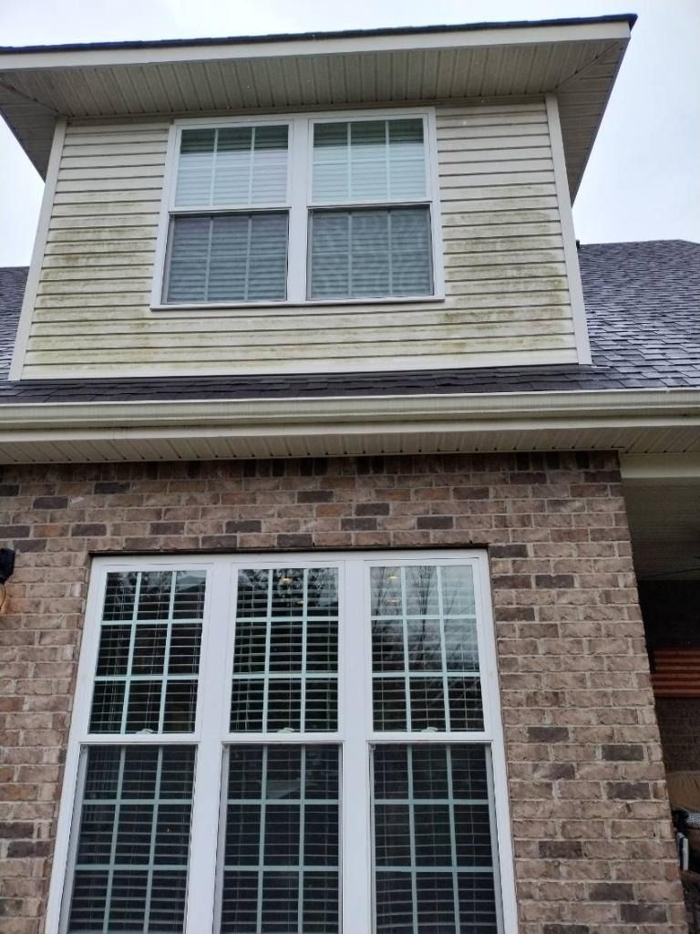 Two-story house exterior with brick lower level, beige siding, and white-trimmed windows