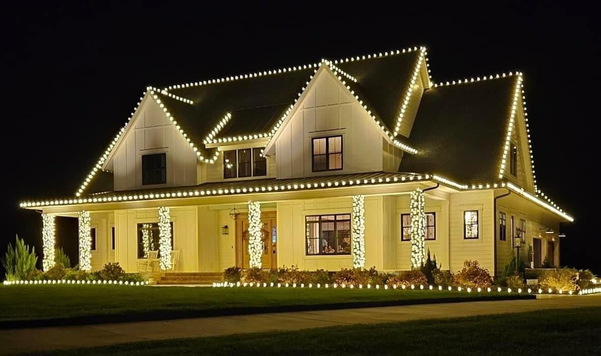 Two-story house outlined with warm white holiday lights at night