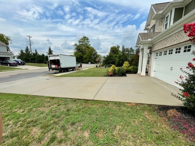 Suburban driveway and front yard beside a garage, with a truck parked on the street under a cloudy sky.