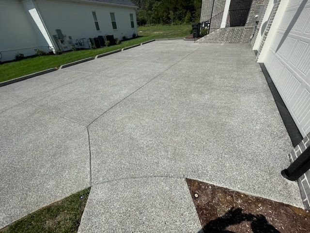 Wide concrete driveway beside a white house, with a brick entryway and green lawn