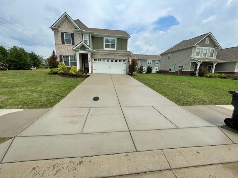 Suburban two-story house with a wide concrete driveway and a lawn under a partly cloudy sky