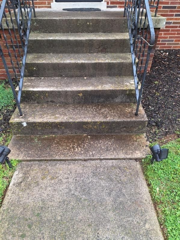 Concrete front steps with black railings leading up from a walkway to a brick building entrance