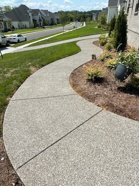 Curved concrete sidewalk beside landscaped homes in a suburban neighborhood on a sunny day
