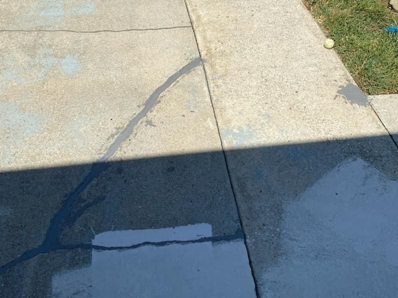 Cracked concrete sidewalk with a dark shadow across it and a small wet patch near the bottom.