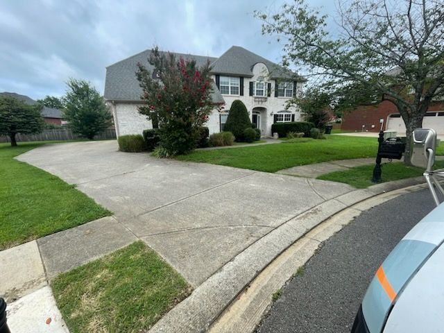 Suburban house with a wide concrete driveway, green lawn, and parked vehicle at the curb