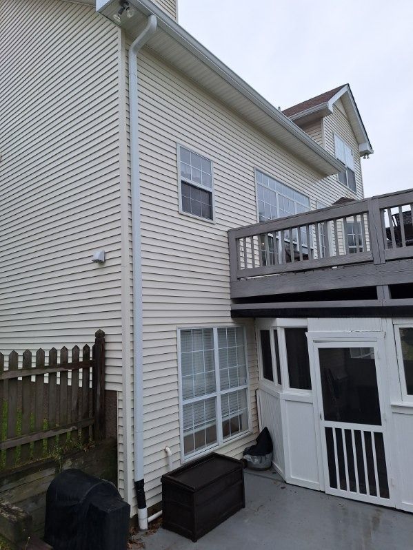 Side view of a beige house with a raised deck, white patio doors, and a fenced yard.