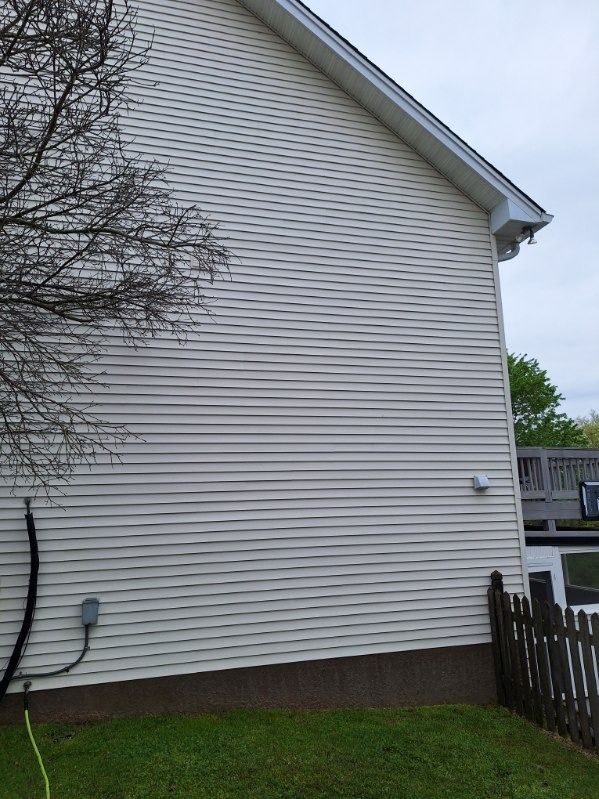 White vinyl-sided house exterior beside a wooden fence and grassy yard under an overcast sky
