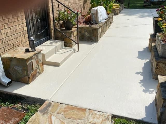 Freshly poured concrete walkway beside a brick house with stone planters and steps