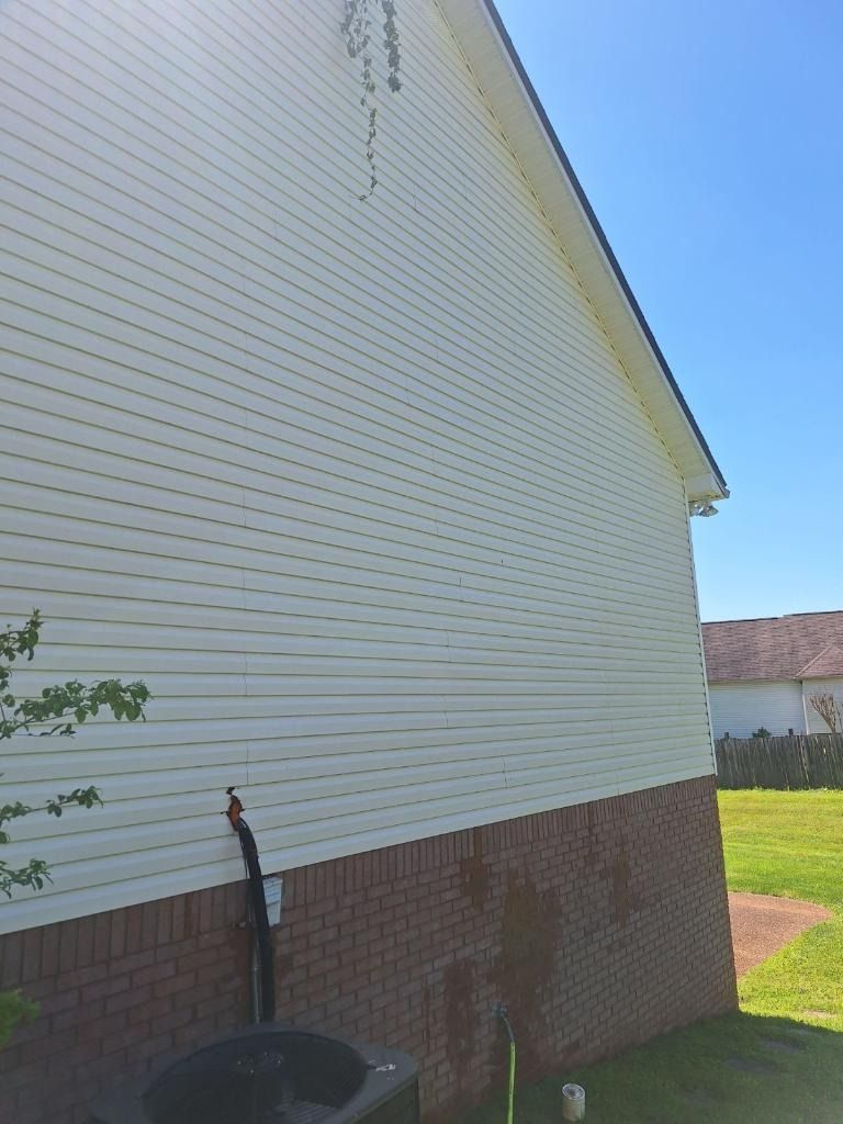 Side view of a house with white siding, brick foundation, a downspout, and a grassy yard.