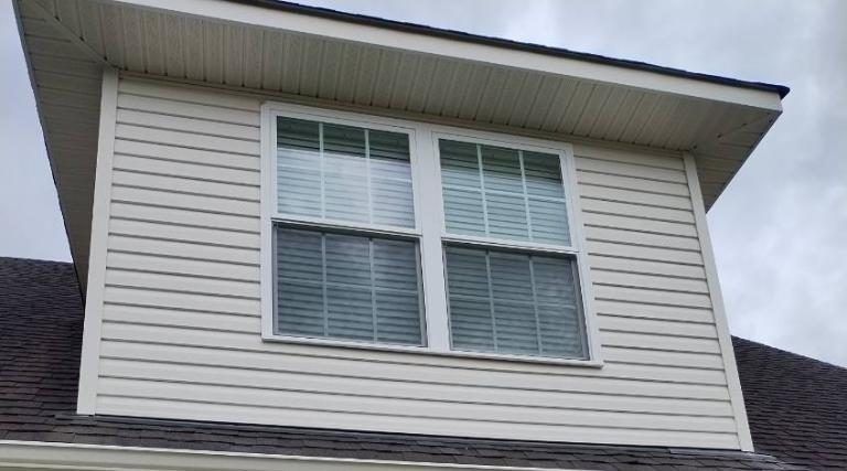 White dormer window with four panes on a house roof under a cloudy sky