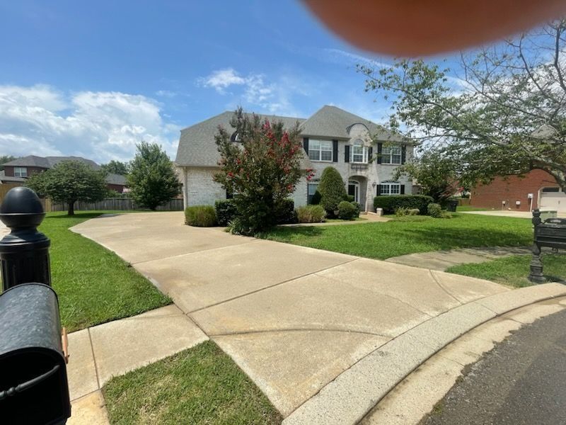Suburban two-story house with a wide driveway, green lawn, and partly cloudy sky