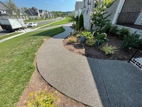 Curved accessible walkway beside an apartment building, bordered by grass and landscaping.