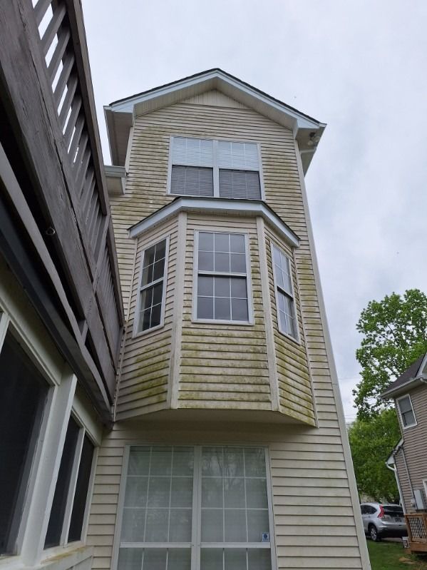 Narrow beige house exterior with a bay window, viewed from below between neighboring buildings.