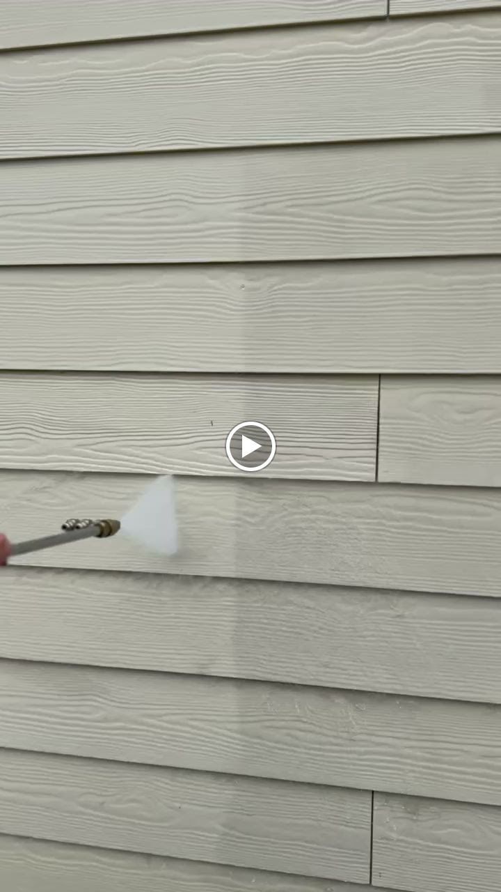 Person spraying cleaner on beige vinyl siding outdoors