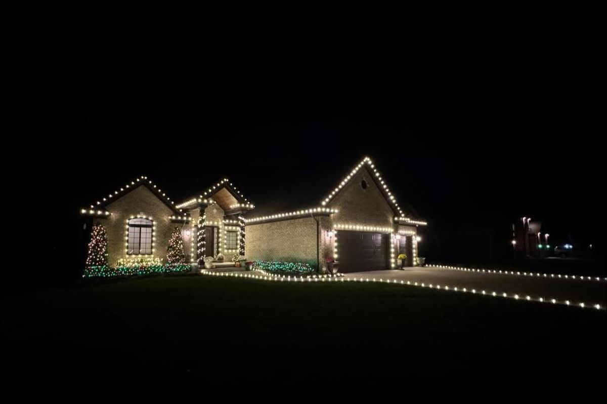 House at night outlined with white holiday lights, with a lit driveway and dark sky.