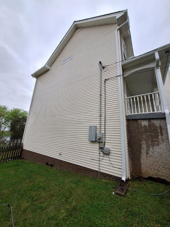 Exterior side of a white house with utility meters and a small covered porch over grass