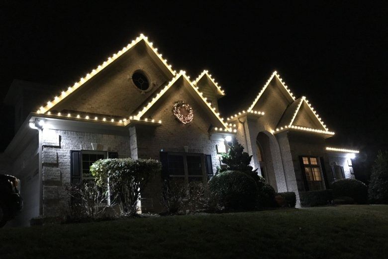 A house at night outlined with warm white roof lights and dark windows in a quiet yard.