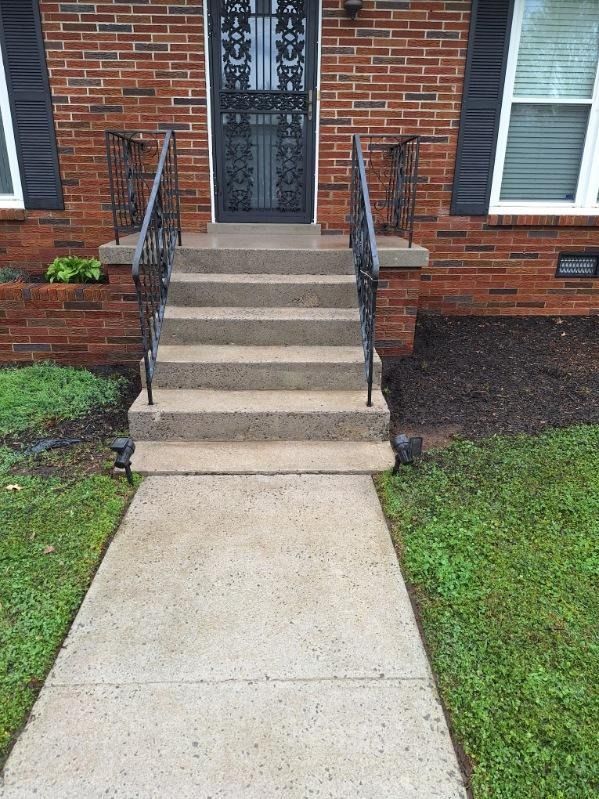 Brick house entrance with concrete steps, metal railings, and a front walkway.
