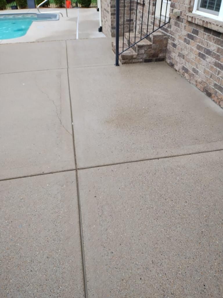 Poolside concrete patio beside a brick house and metal gate