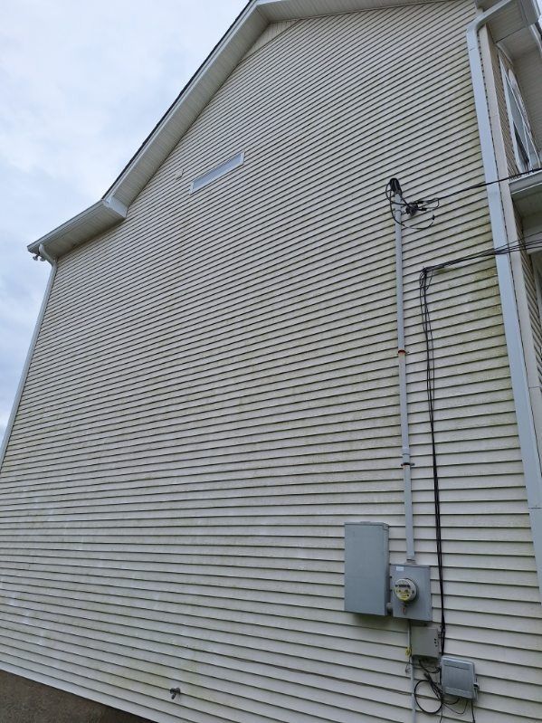 Side of a beige vinyl-sided house with utility meter and conduit lines near the foundation