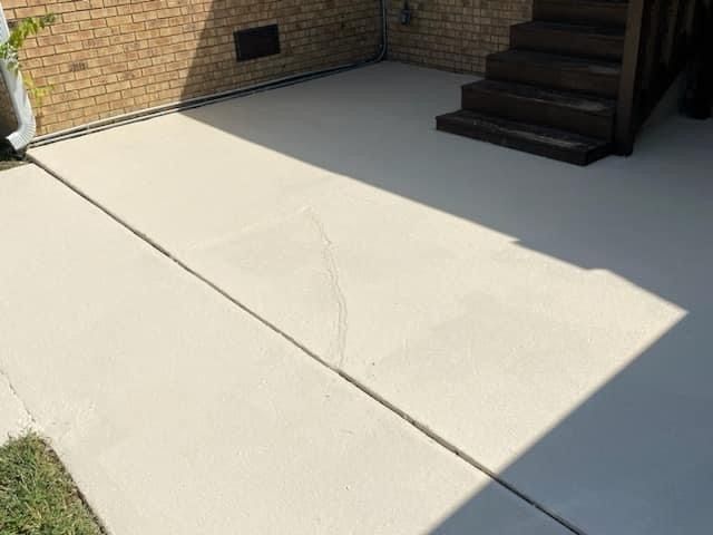 Concrete patio beside brick wall and steps, with a diagonal expansion joint and strong sunlight/shadow.