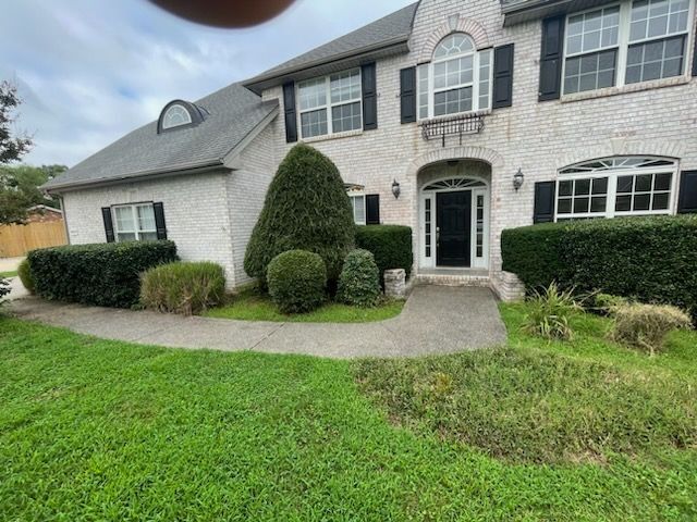 Two-story suburban house with white brick, arched front door, trimmed hedges, and a green lawn