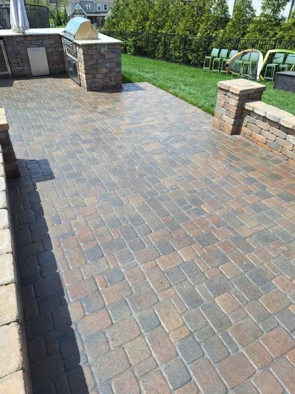 Brick patio walkway beside a green lawn and stone pillars in a sunny yard