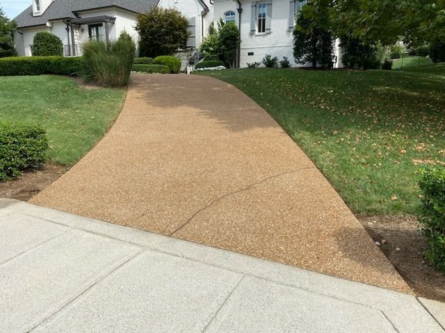 Front walkway leading to a white house, with a tan driveway and green lawn on both sides