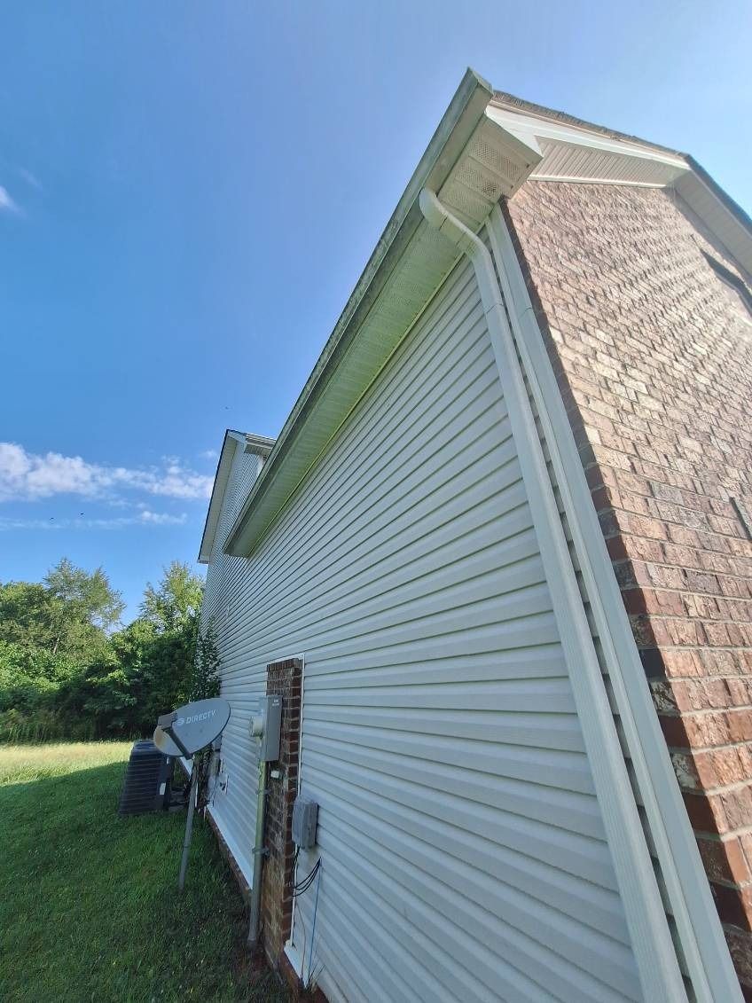 White vinyl-sided house exterior with tan brick corner, viewed from the side under a blue sky