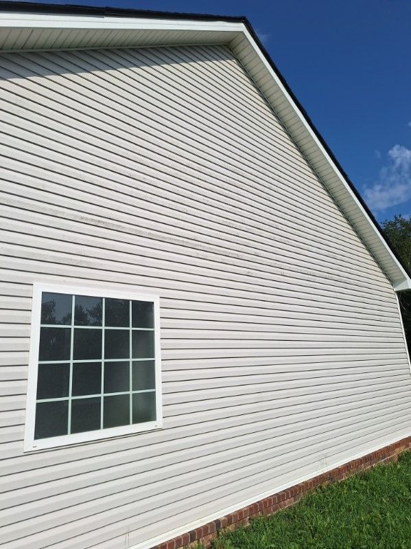 White vinyl house siding with a window under a blue sky, viewed from the side