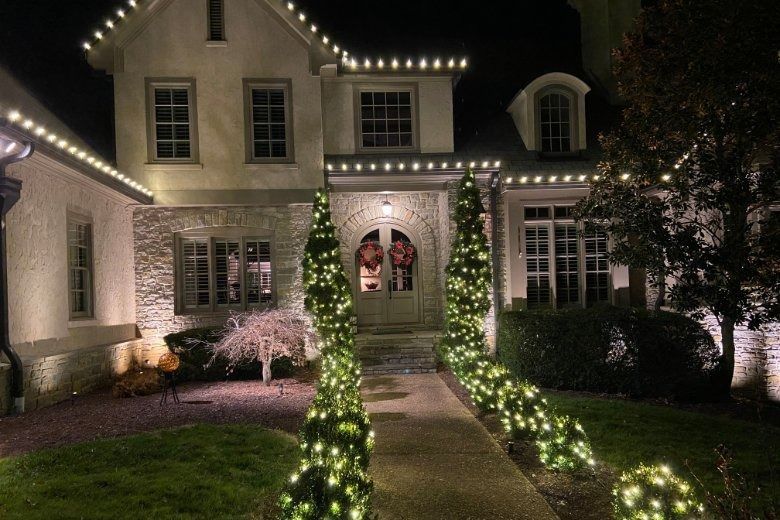House at night outlined with white holiday lights and illuminated greenery along the walkway.