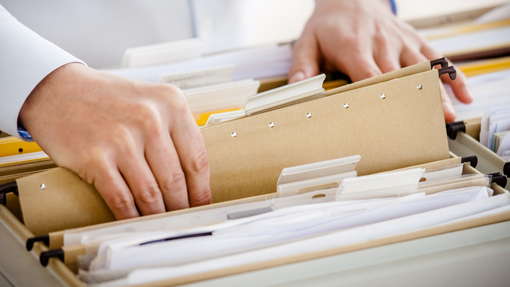 A person is looking through a filing cabinet full of papers.