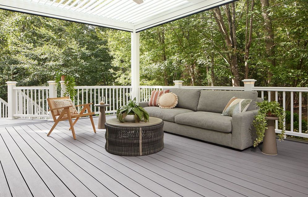 Gray deck with white railing, sofa, and chair overlooking trees.